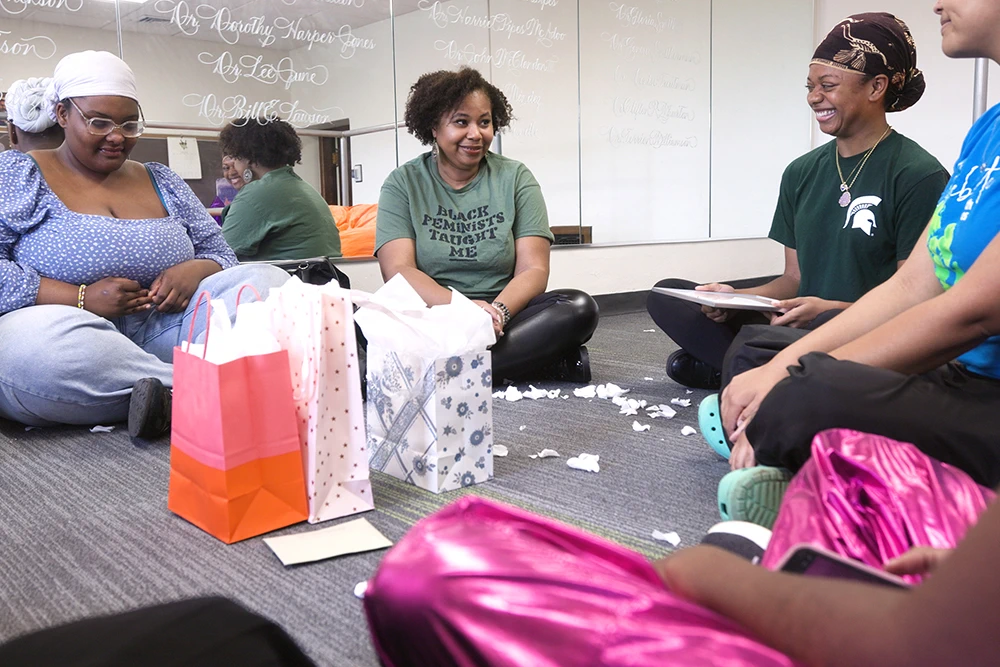 A group of women sit on the floor and talk with each other. Mirrors in the background reflecting their interactions.