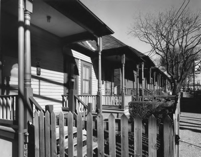 Wooden fencing surrounds the small yards and porches in front of a row of shotgun homes. Wooden fencing surrounds the small yards and porches in front of a row of shotgun homes.
