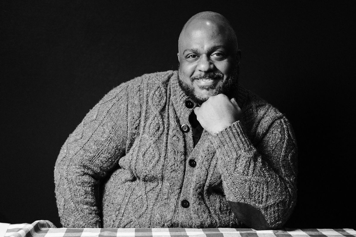Black and white photo of Lorenzo Wyche smiling in a warm cardigan, a Black Atlanta chef and co-owner in the Breakfast Boys in Atlanta. 