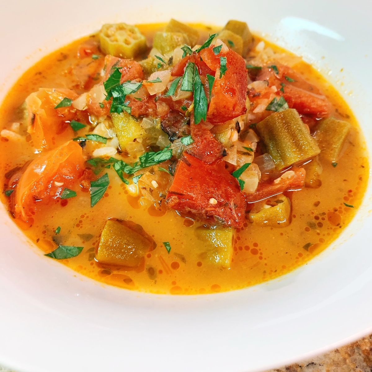 A white bowl contains a burnt orange broth filled with chunks of fresh tomotes and okra from Liz and Leon’s in Atlanta. 