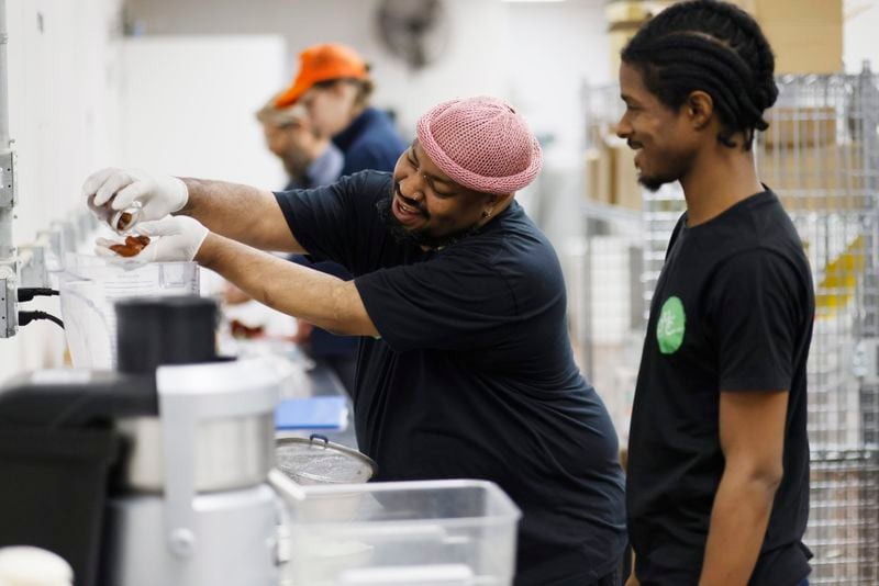 Antonio Little (left) adds dates to his pecan milk while his co-worker Nil Jones looks on. They are part of a company co-owned by six employees called Pekan Milk Cooperative, which produces various milk, including pecan, oat, hemp, and sunflower milk. Thursday, April 13, 2023.Miguel Martinez /miguel.martinezjimenez@ajc.com